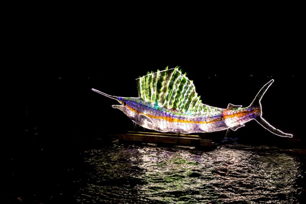 Swordfish made from recycled plastic bottles lit up in many different colors at night on the water